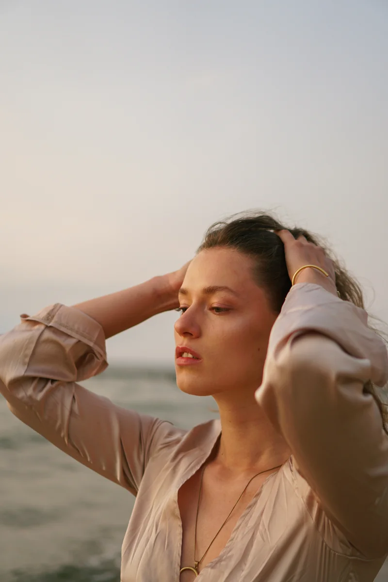 Portrait mit angehobenen Haenden am Strand im warmen Licht